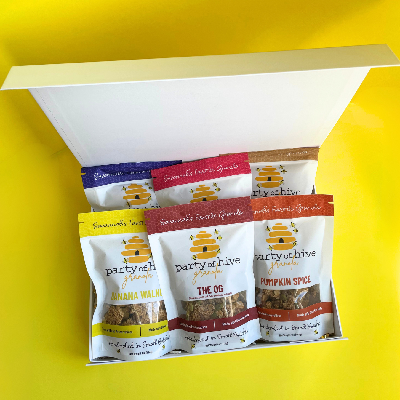 Assorted granola packages from 'party of hive' in a box on a yellow background