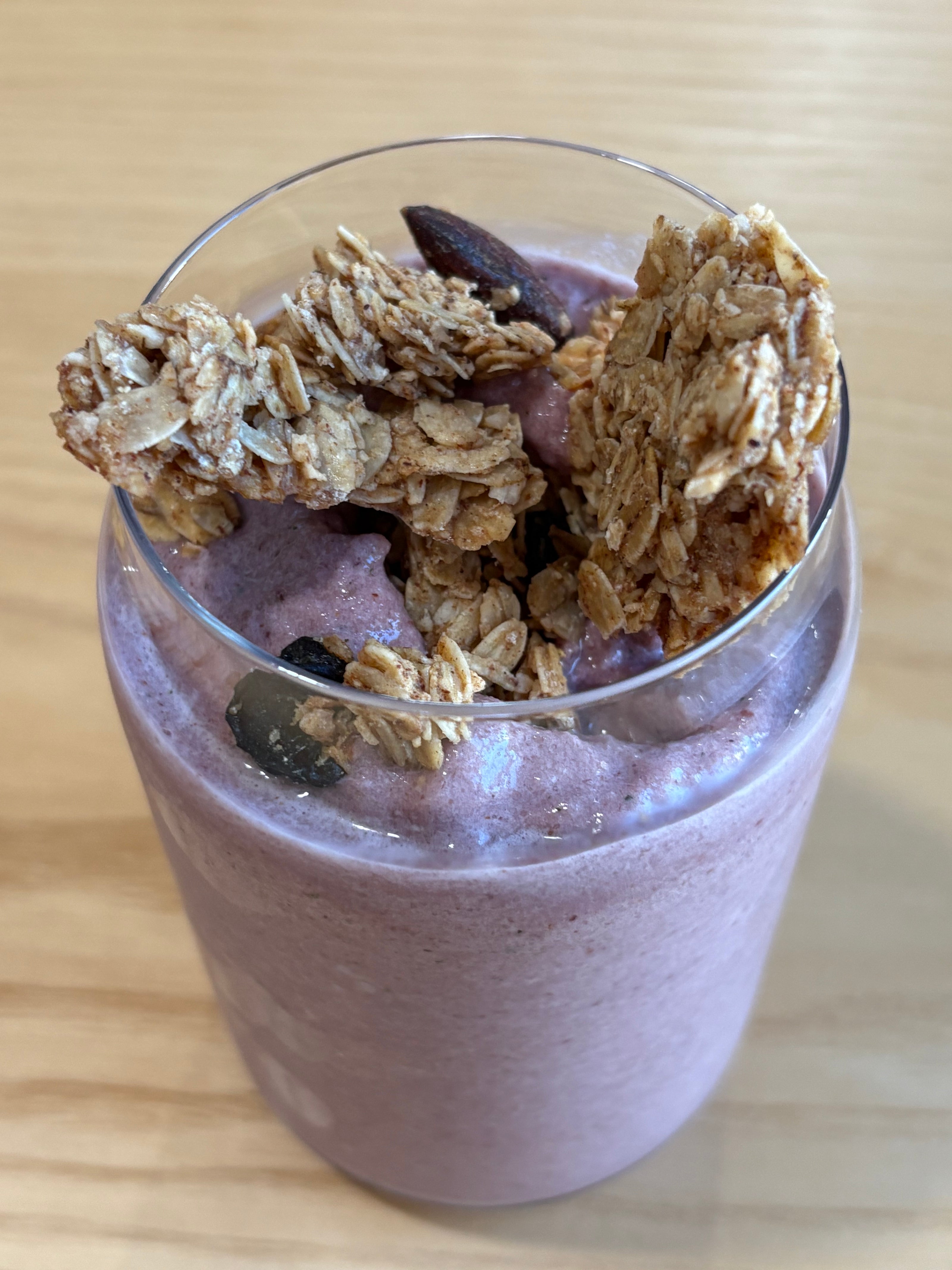 smoothie in a glass with granola on a wooden surface